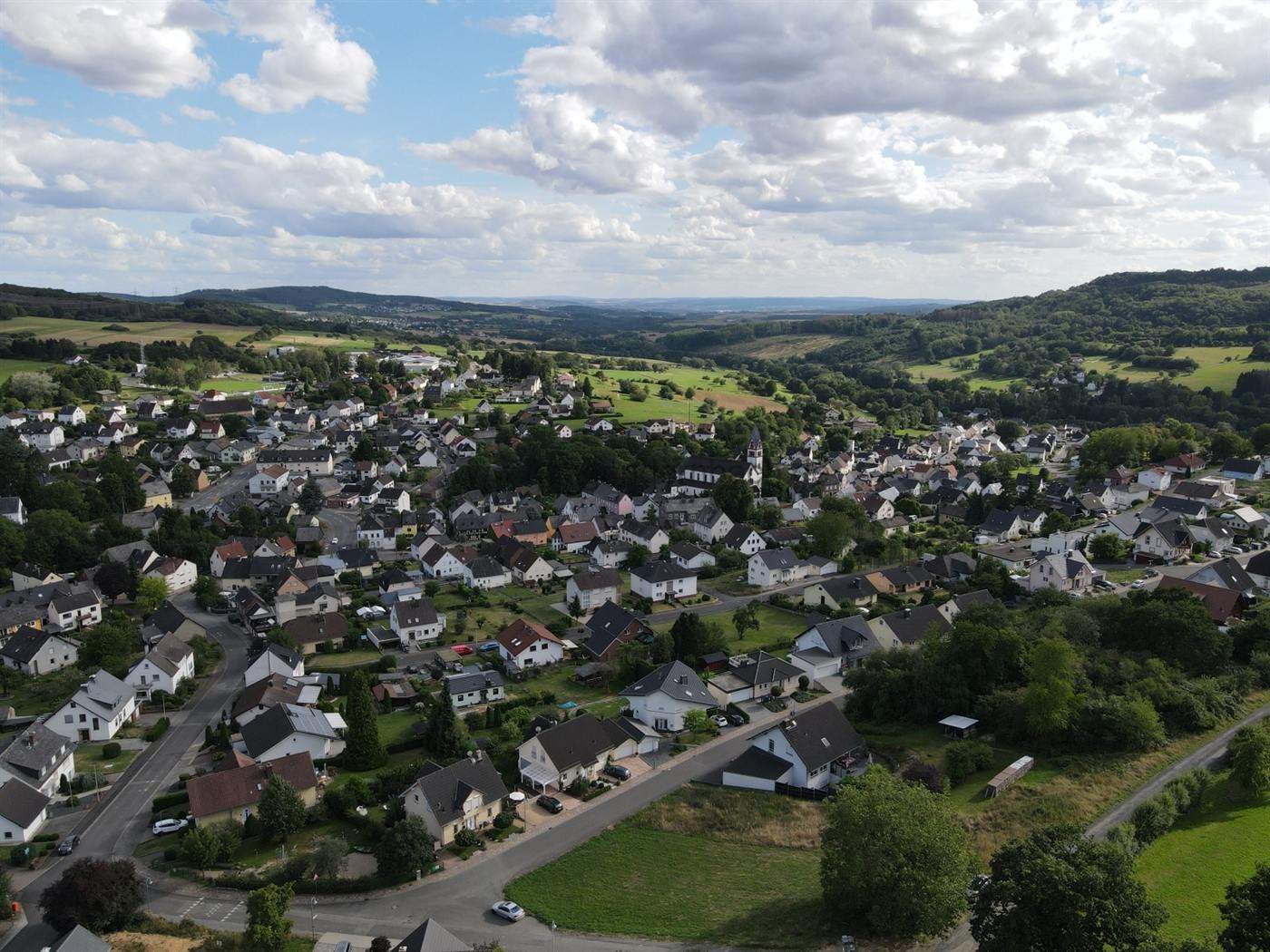 Luftbild über die Dächer von Langendernbach mit dem Kirchturm und den umliegenden Feldern.