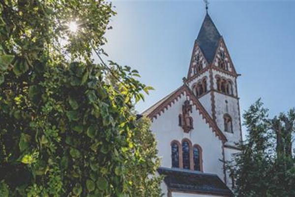 Der Turm der Pfarrkirche St. Matthias mit Rundbogenfenstern und spitzem Helm, umrahmt von Baumblättern.