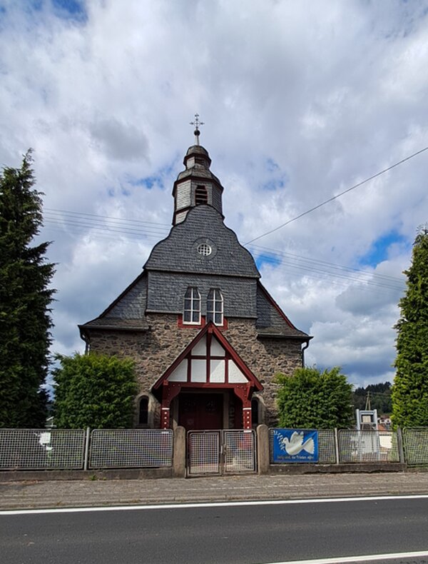 Die evangelische Kapelle Langendernbach mit verschiefertem Turm und rot-weißem Fachwerkgiebel am Eingang.